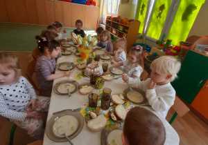 Dzieci siedzą przy wspólnym stole i jedzą śniadanie wielkanocne